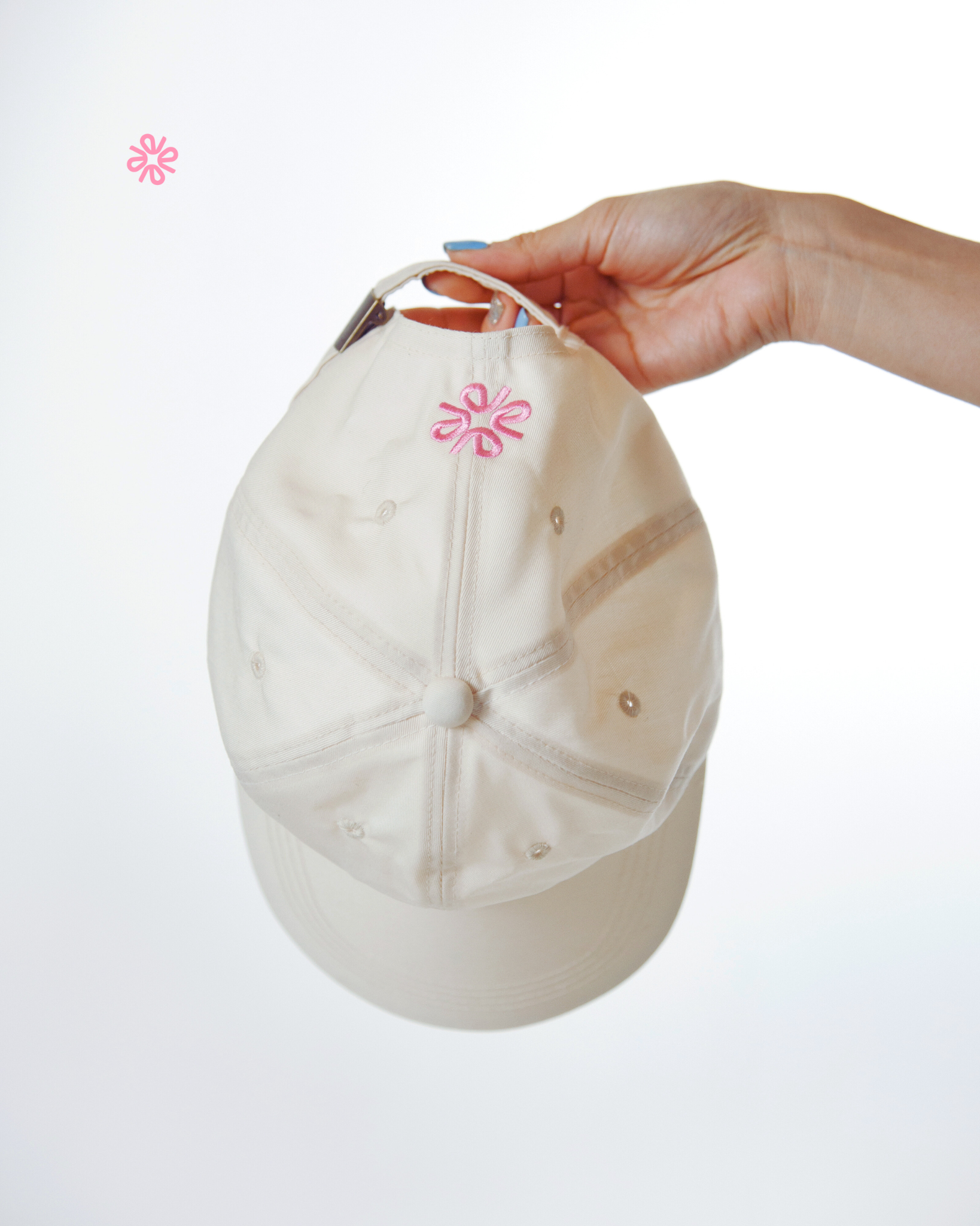 Beige cap with a pink logo held by a hand on a white background